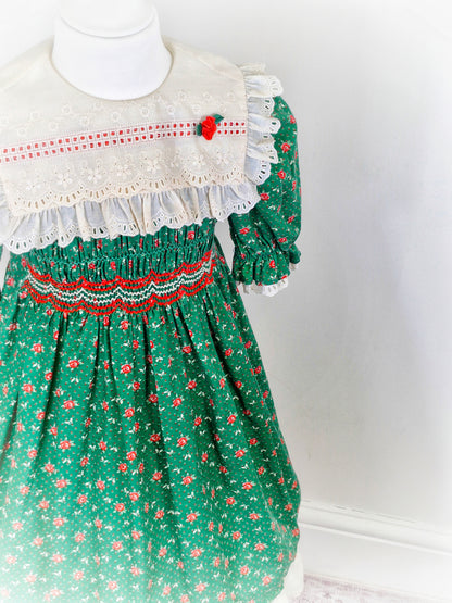 6-7 years. Vintage Polly Flinders smock dress, forest green with cream eyelet bib embroidered with flowers and red embroidered smocking