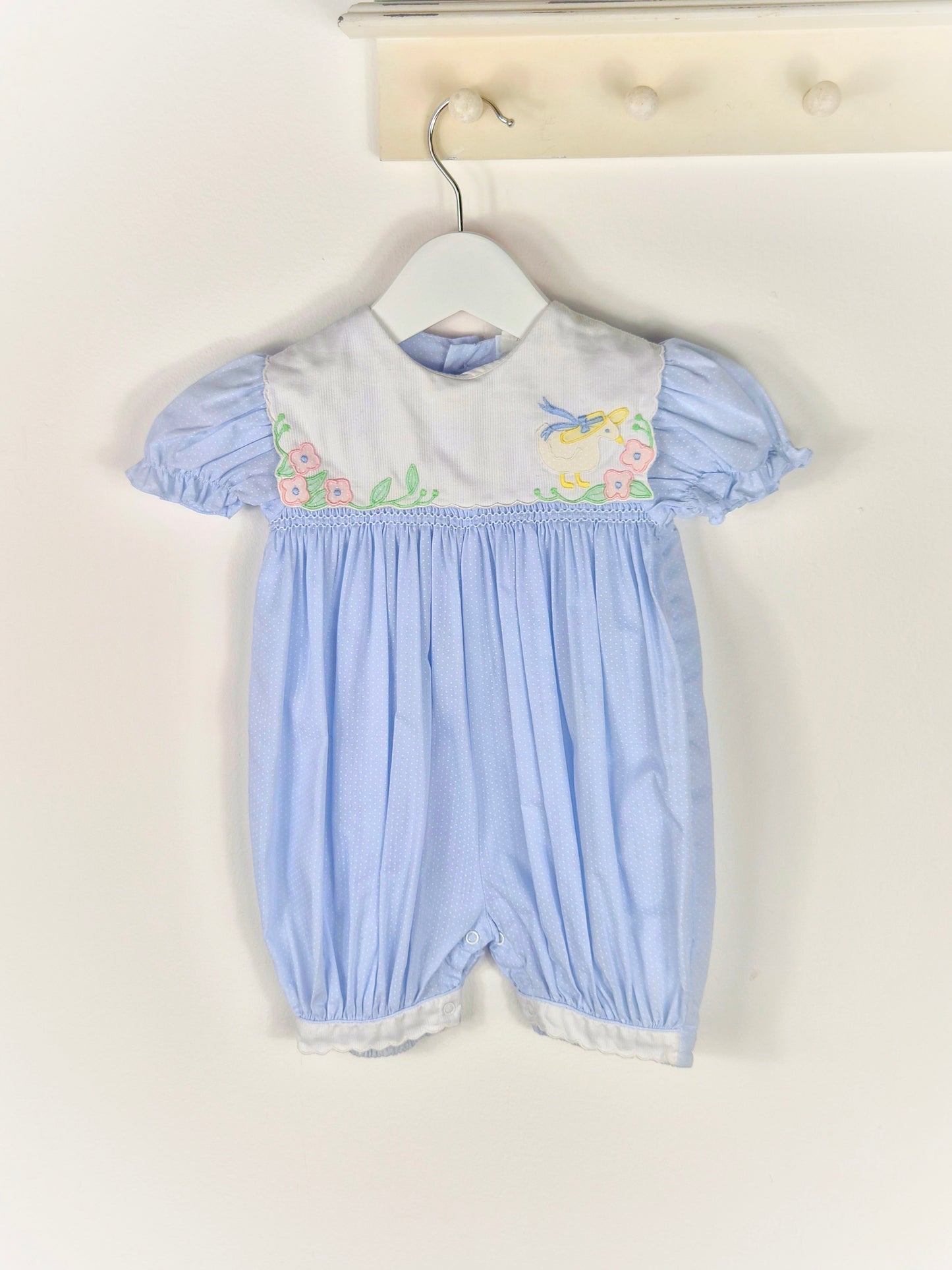 9-12 months. Blue polka dot, smocked, short vintage romper with puff sleeves and white bib embroidered with a duck in a hate and flowers