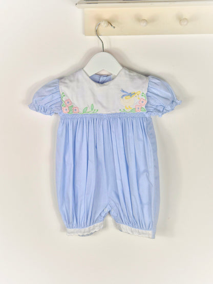 9-12 months. Blue polka dot, smocked, short vintage romper with puff sleeves and white bib embroidered with a duck in a hate and flowers