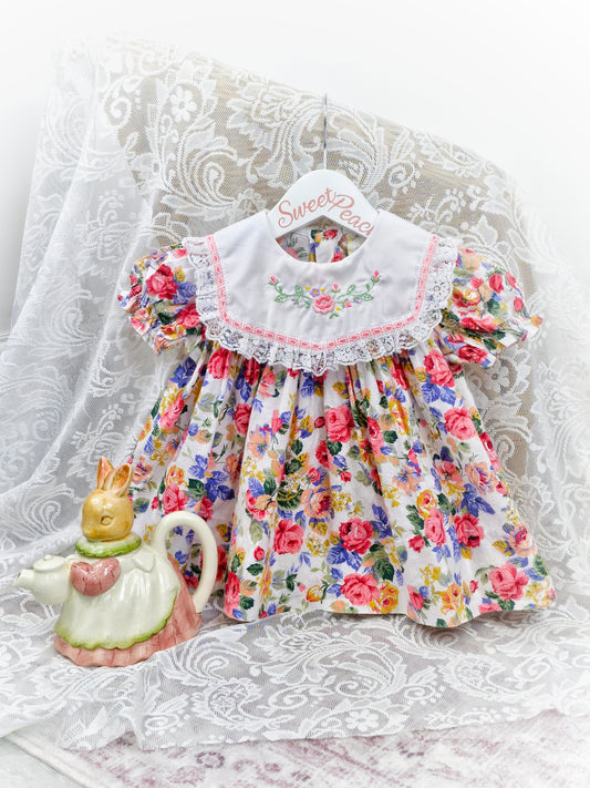 9-12 months. Floral dress with white bib embroidered with flowers and finished with lace