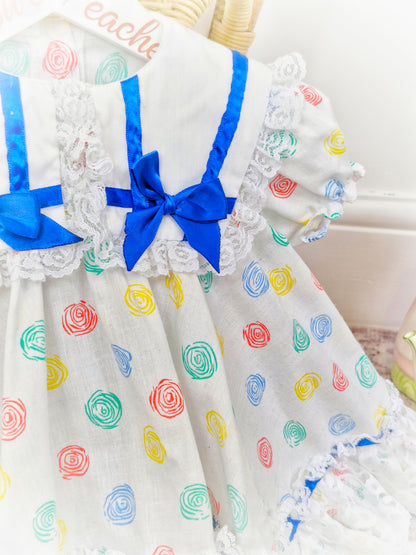12-18 months. White Kotton Kandi dress with royal blue ribbon, lace and primary coloured prints
