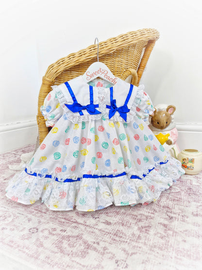 12-18 months. White Kotton Kandi dress with royal blue ribbon, lace and primary coloured prints