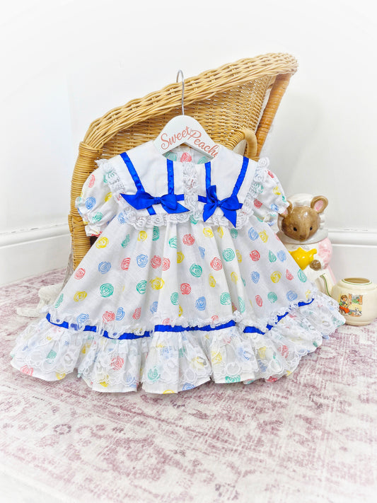 12-18 months. White Kotton Kandi dress with royal blue ribbon, lace and primary coloured prints