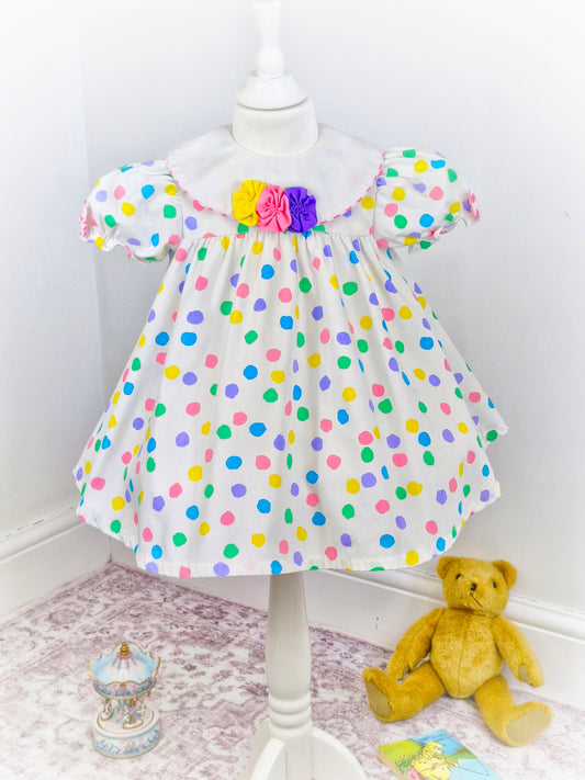 2-3 years. White dress with bright coloured spots and detailed bib