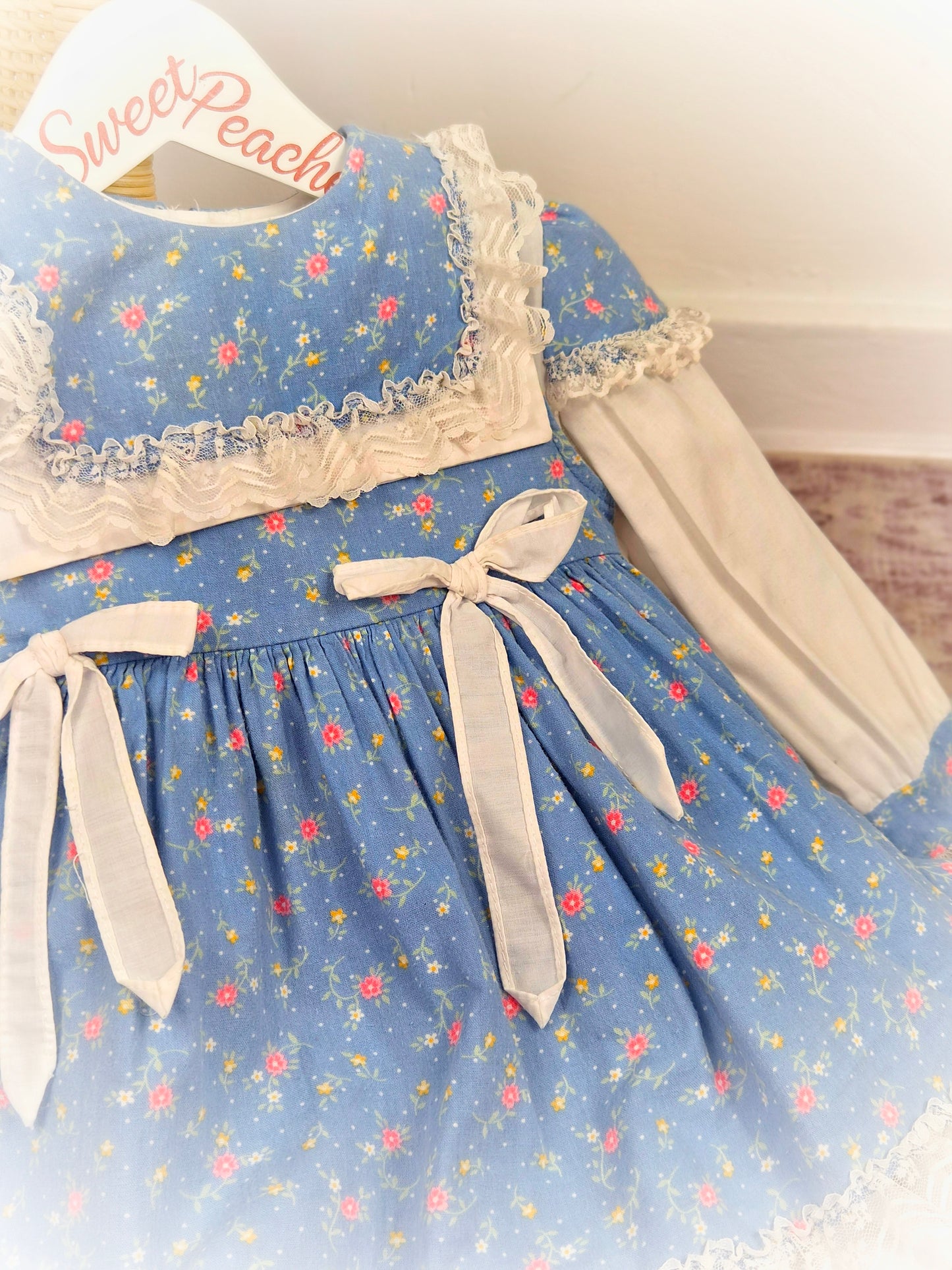18-24 months. Blue Two-piece vintage dress and pinny with white bow, floral print and lace details