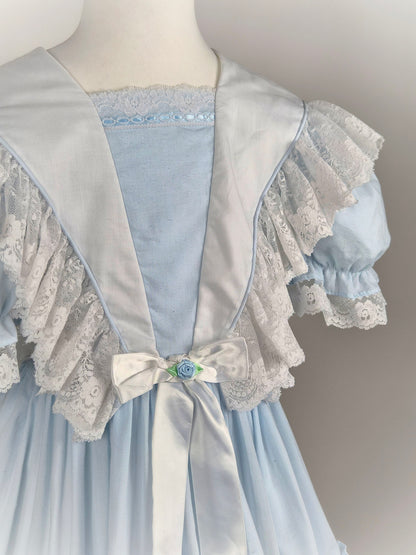 7-8 years. Blue vintage dress with white lace frills and trim, white satin ribbon and blue rosette