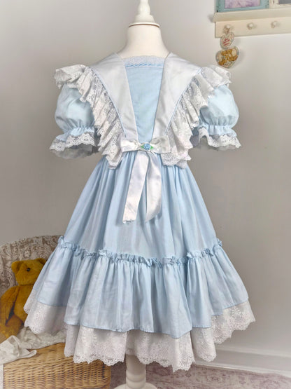 7-8 years. Blue vintage dress with white lace frills and trim, white satin ribbon and blue rosette