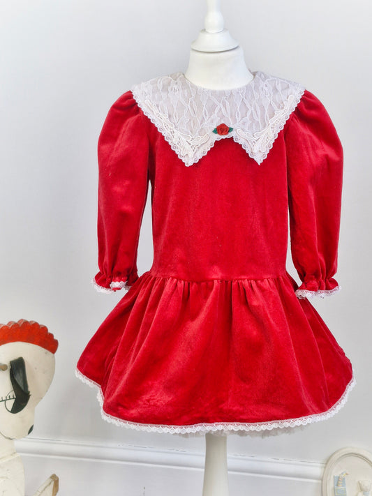 5 years. Red velour dress, white lace bib and trim