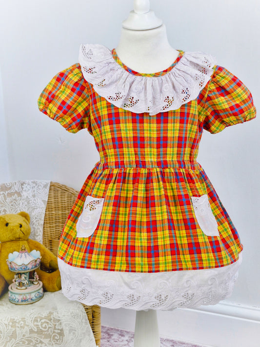 3 years. Checked dress, with white embroidered bib, pockets and hem. yellow orange blue
