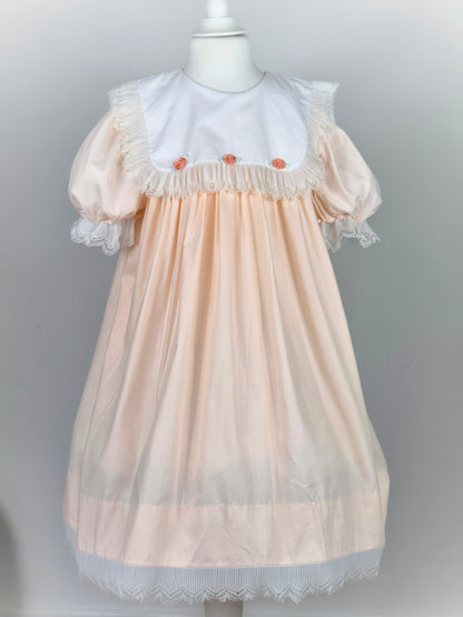 8-9 years. Peach vintage dress with white bib, lace trim and 3 peach coloured rosettes