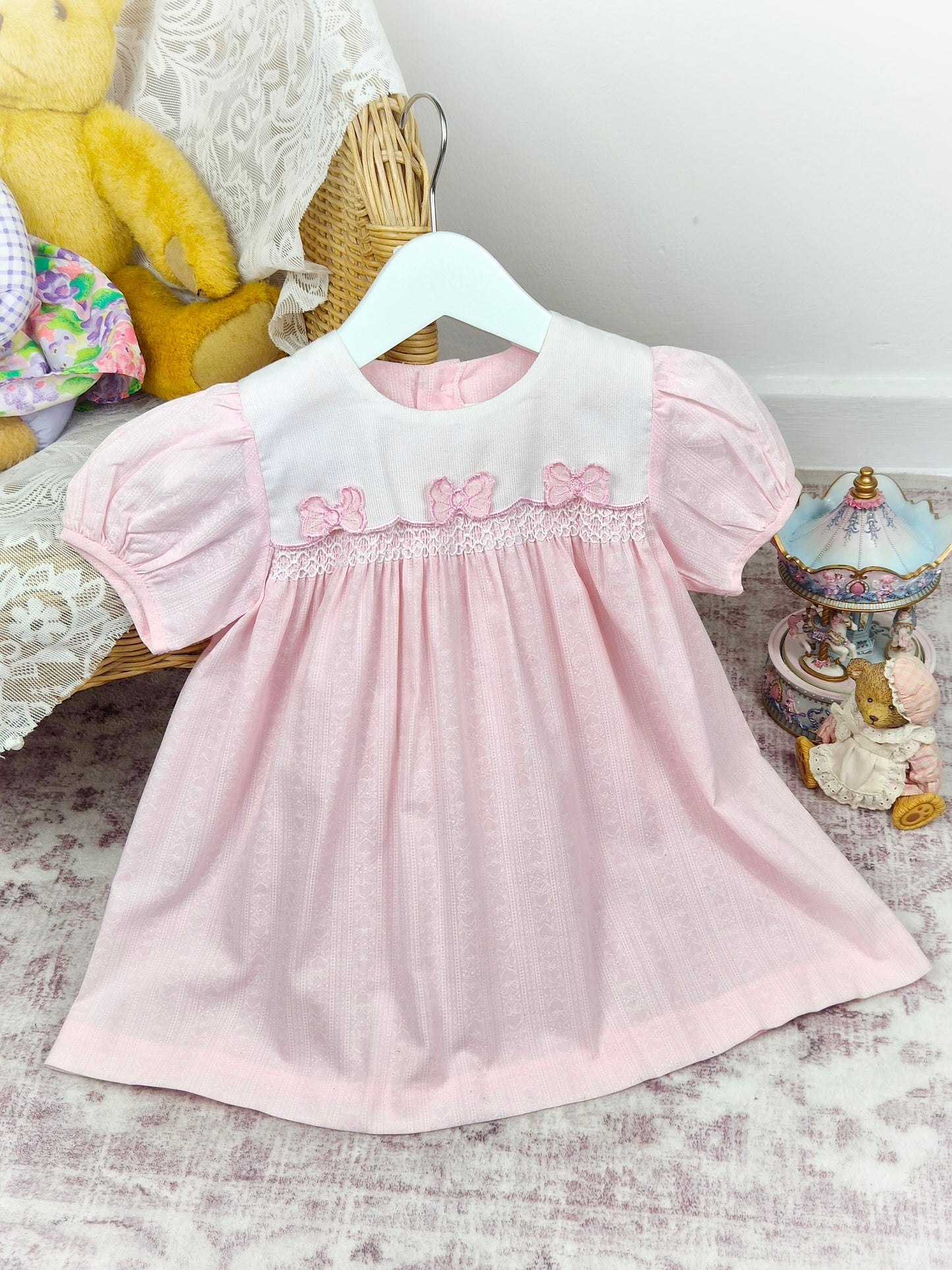 2 years. Pink vintage smocked dress by Maude Wilson with white bib, floral print and three pink bows