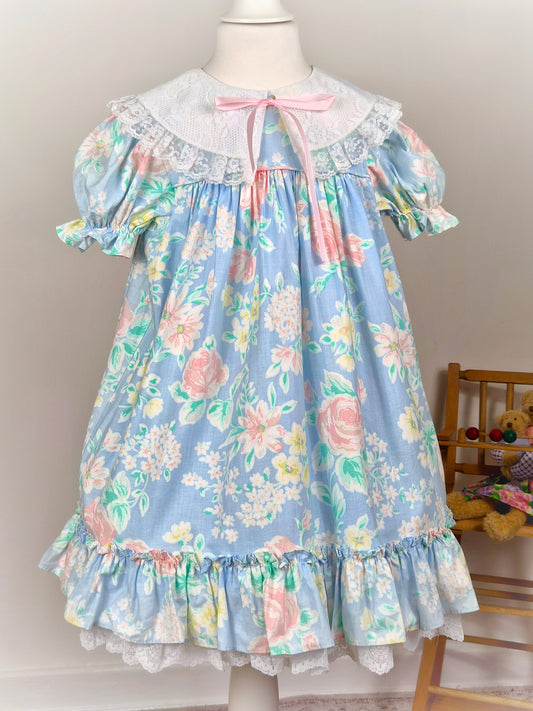 5 years. Blue floral vintage Bryan dress with white lace bib and hem and pink ribbon. Small faults*