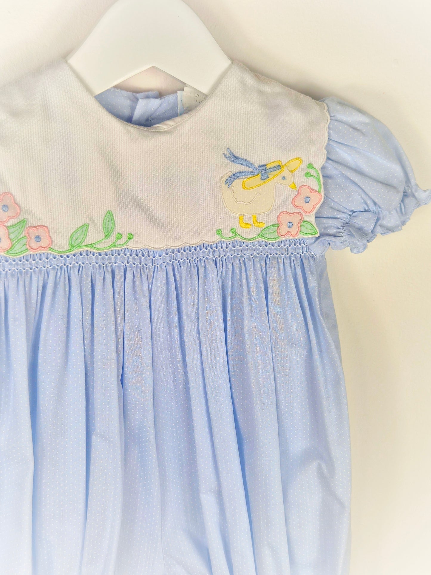 9-12 months. Blue polka dot, smocked, short vintage romper with puff sleeves and white bib embroidered with a duck in a hate and flowers